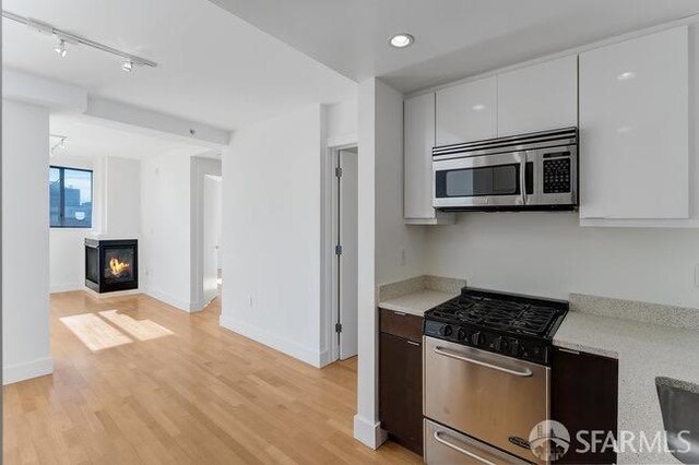 kitchen with track lighting, white cabinets, a wood stove, light hardwood / wood-style flooring, and appliances with stainless steel finishes