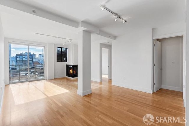 unfurnished living room featuring rail lighting, a wood stove, and hardwood / wood-style flooring