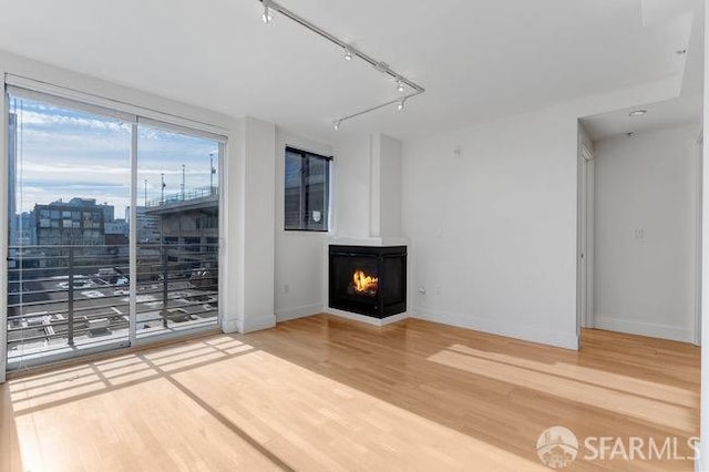 unfurnished living room featuring wood-type flooring, a wood stove, and rail lighting