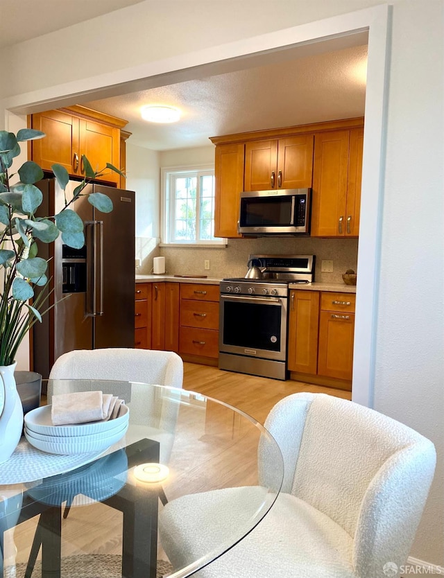 kitchen featuring light countertops, decorative backsplash, light wood-style flooring, brown cabinets, and stainless steel appliances