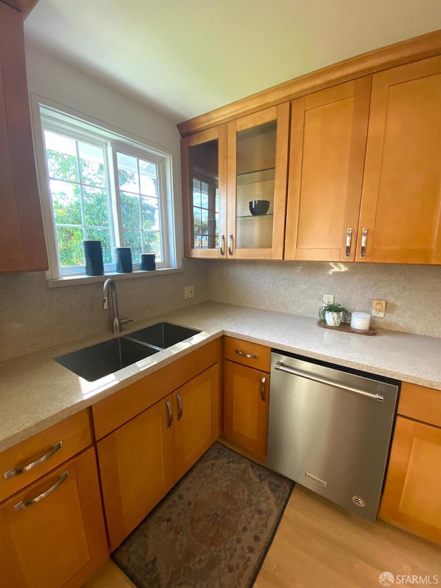 kitchen featuring backsplash, glass insert cabinets, dishwasher, light countertops, and a sink