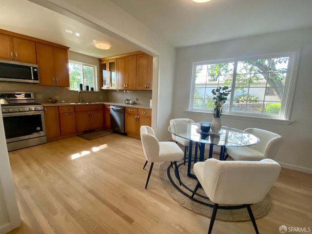 kitchen with light wood finished floors, appliances with stainless steel finishes, brown cabinetry, and a sink