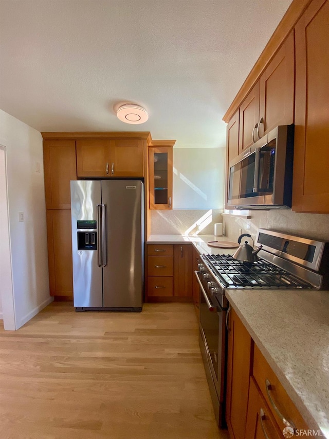 kitchen featuring stainless steel appliances, brown cabinets, glass insert cabinets, and light wood finished floors