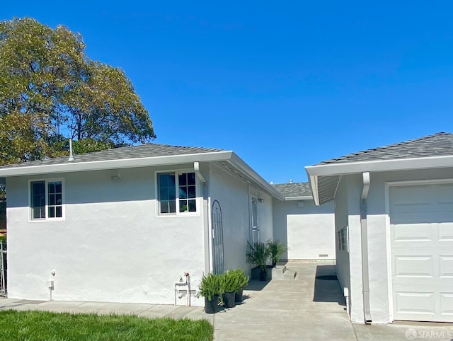 view of side of property with stucco siding, an attached garage, and a shingled roof