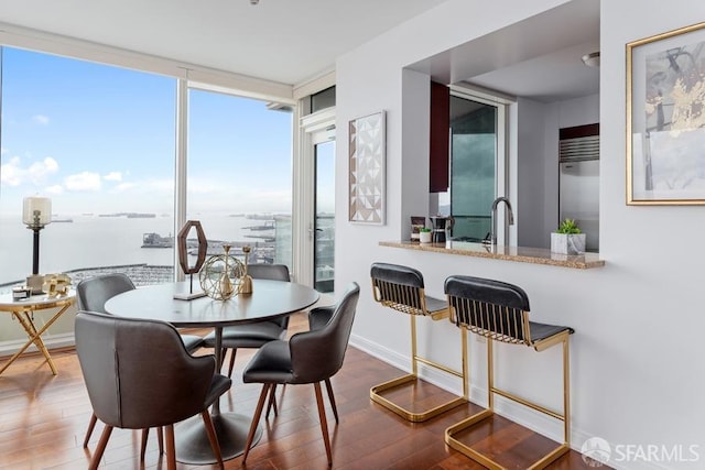 dining area featuring hardwood / wood-style flooring, a wall of windows, and a water view