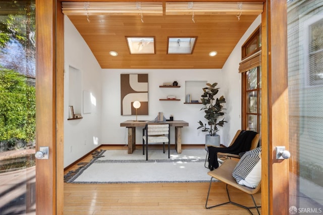 interior space featuring baseboards, lofted ceiling with skylight, wood ceiling, and wood finished floors