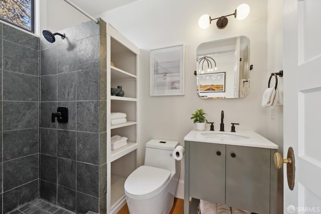 bathroom featuring toilet, tiled shower, and vanity