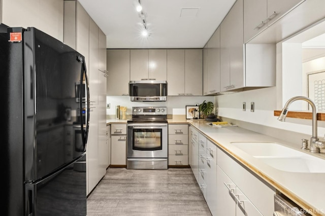 kitchen with gray cabinetry, track lighting, sink, appliances with stainless steel finishes, and light hardwood / wood-style floors