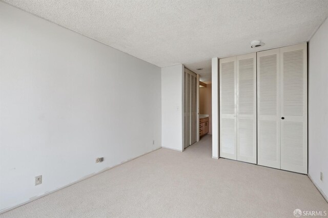 unfurnished bedroom featuring light carpet, a textured ceiling, and a closet