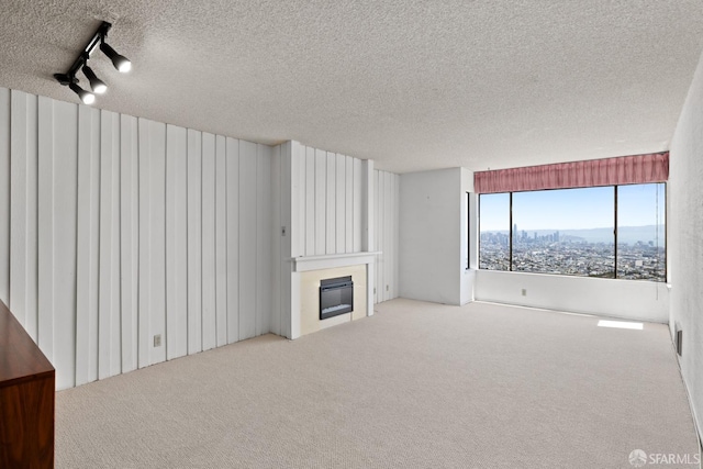 unfurnished living room featuring a textured ceiling, rail lighting, and carpet flooring