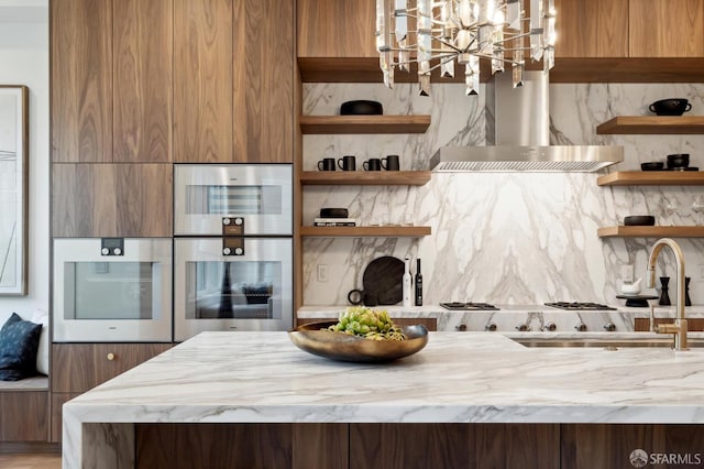 kitchen with sink, stainless steel double oven, wall chimney exhaust hood, and tasteful backsplash