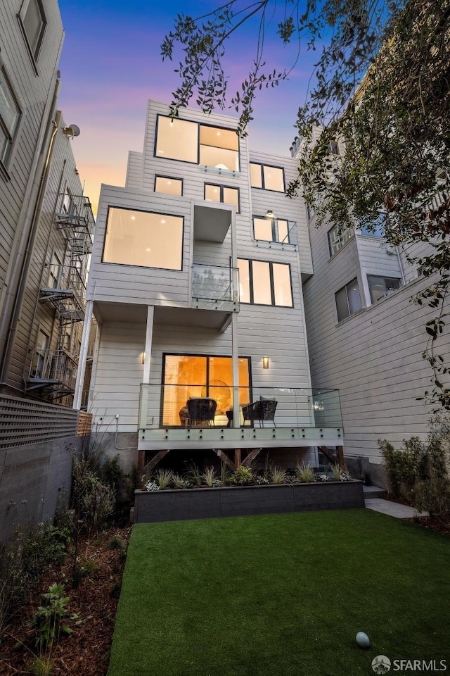 back house at dusk with a balcony and a lawn