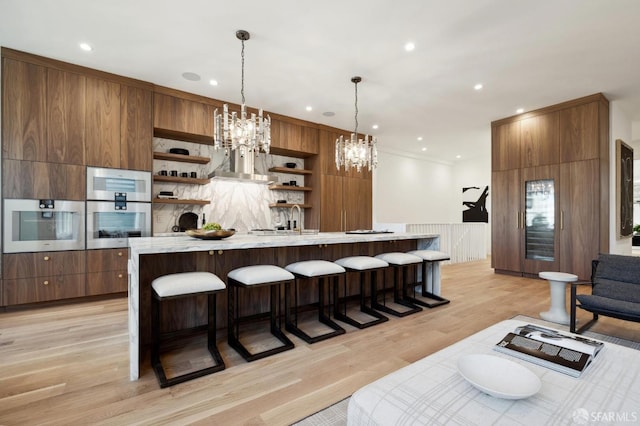 kitchen featuring decorative light fixtures, sink, light wood-type flooring, a breakfast bar, and a large island with sink