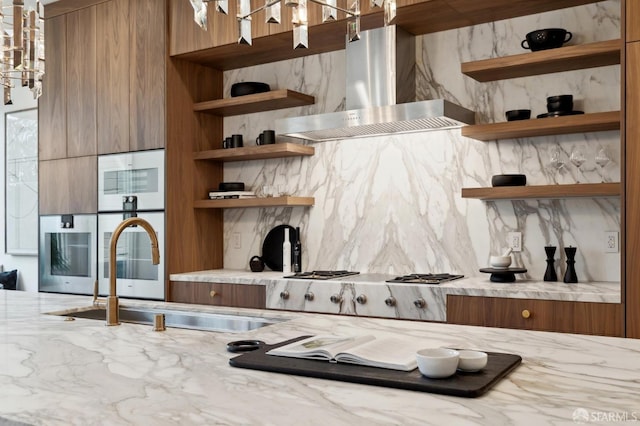 kitchen featuring sink, light stone counters, stainless steel gas stovetop, and wall chimney exhaust hood