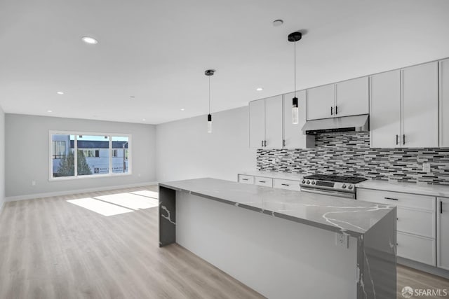 kitchen with tasteful backsplash, under cabinet range hood, light wood finished floors, and gas range