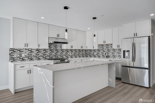 kitchen with under cabinet range hood, stainless steel appliances, white cabinets, a center island, and light wood finished floors