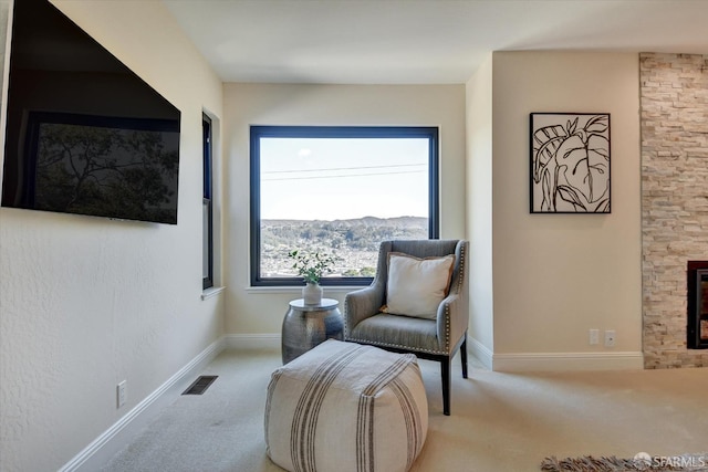 sitting room featuring light colored carpet, a stone fireplace, and a mountain view