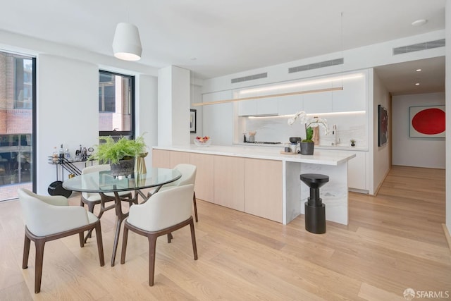 kitchen with white cabinets, decorative backsplash, hanging light fixtures, light hardwood / wood-style floors, and kitchen peninsula