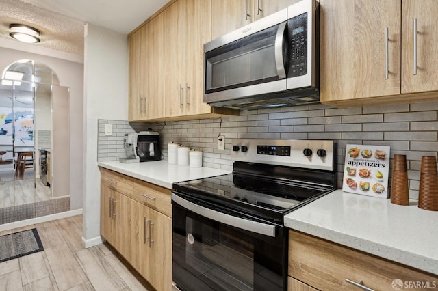 kitchen featuring appliances with stainless steel finishes, decorative backsplash, light brown cabinets, a textured ceiling, and light stone counters