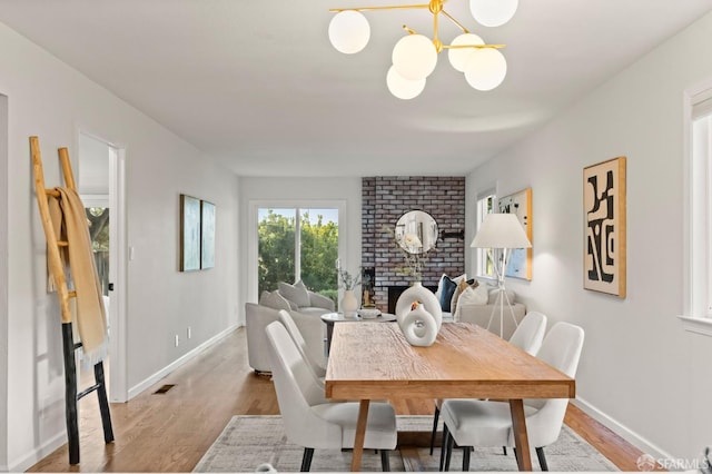 2811 Bayview Dr, Alameda, CA 94501 - dining room with a chandelier, light wood-type flooring, baseboards, and a brick fireplace