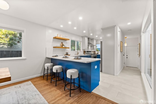 2811 Bayview Dr, Alameda, CA 94501 - kitchen featuring stainless steel gas stove, wall chimney range hood, a breakfast bar area, a peninsula, and light countertops