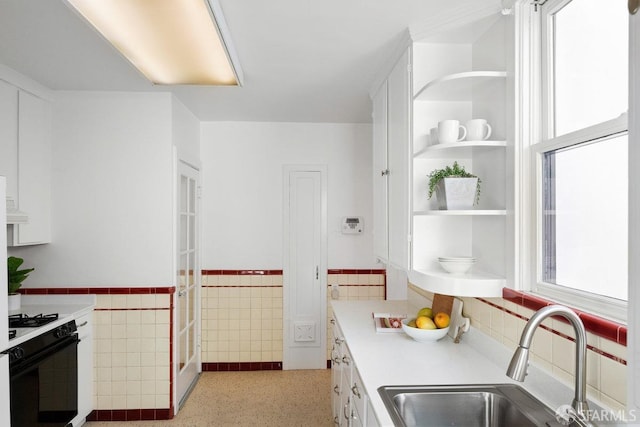 kitchen with white cabinetry, range with gas stovetop, sink, and tile walls