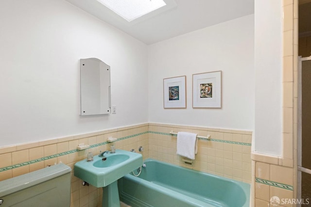 bathroom featuring toilet, a skylight, a bathing tub, and tile walls