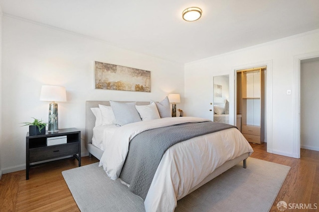 bedroom featuring crown molding, a closet, a spacious closet, and light hardwood / wood-style flooring