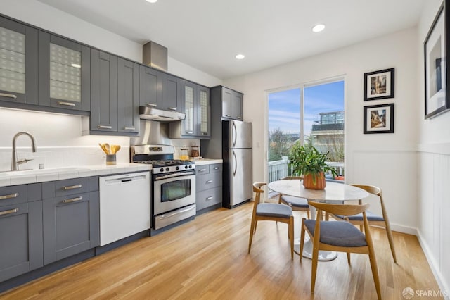 kitchen featuring sink, gray cabinetry, tile countertops, light wood-type flooring, and stainless steel appliances