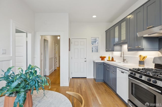 kitchen with tasteful backsplash, sink, white dishwasher, stainless steel range with gas stovetop, and light hardwood / wood-style flooring