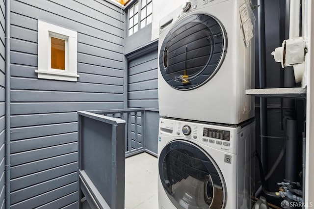 clothes washing area with wooden walls and stacked washer and clothes dryer