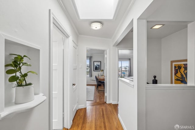 corridor with light wood-style floors, crown molding, and baseboards