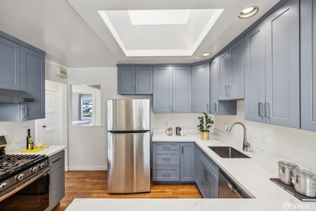 kitchen featuring light wood-style flooring, appliances with stainless steel finishes, light stone counters, under cabinet range hood, and a sink