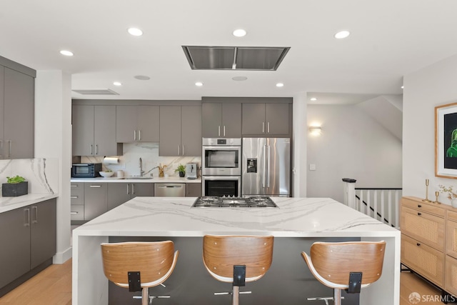 kitchen with appliances with stainless steel finishes, a kitchen island, a breakfast bar area, and gray cabinetry