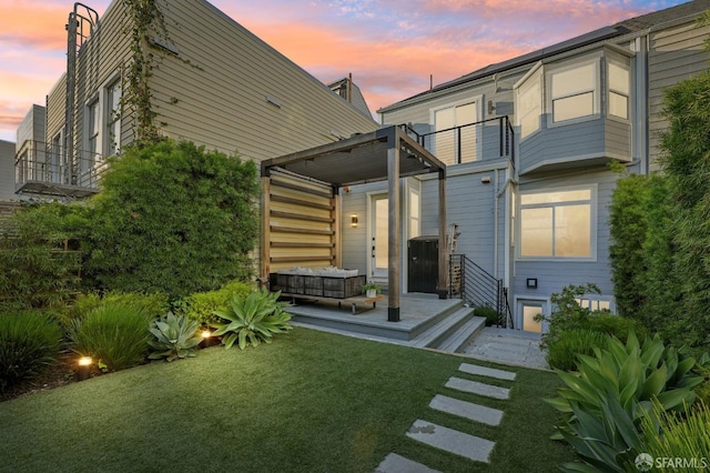 back house at dusk featuring a balcony and a yard