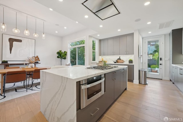 kitchen with decorative light fixtures, light hardwood / wood-style flooring, appliances with stainless steel finishes, gray cabinets, and a kitchen island