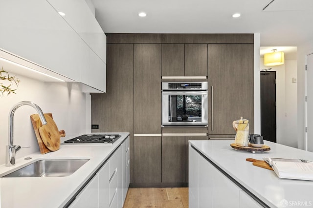 kitchen featuring dark brown cabinetry, sink, white cabinetry, light hardwood / wood-style flooring, and stainless steel appliances