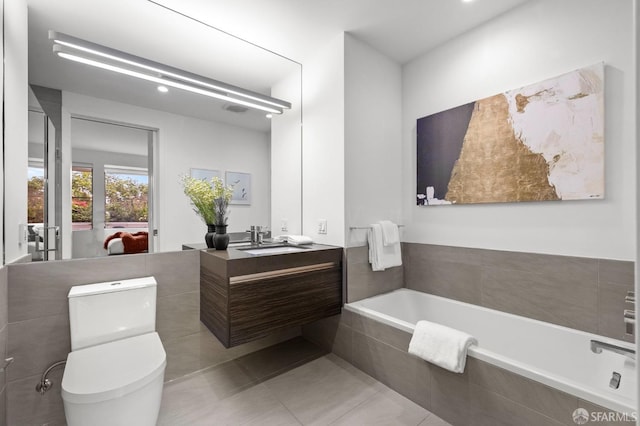 bathroom featuring tiled tub, vanity, tile patterned flooring, and toilet