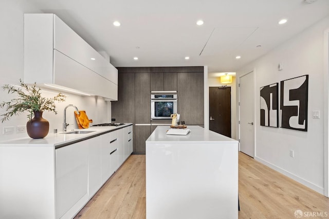 kitchen featuring sink, stainless steel oven, a center island, gas cooktop, and light hardwood / wood-style floors