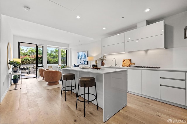 kitchen with a kitchen island, stainless steel gas cooktop, white cabinets, and light hardwood / wood-style flooring