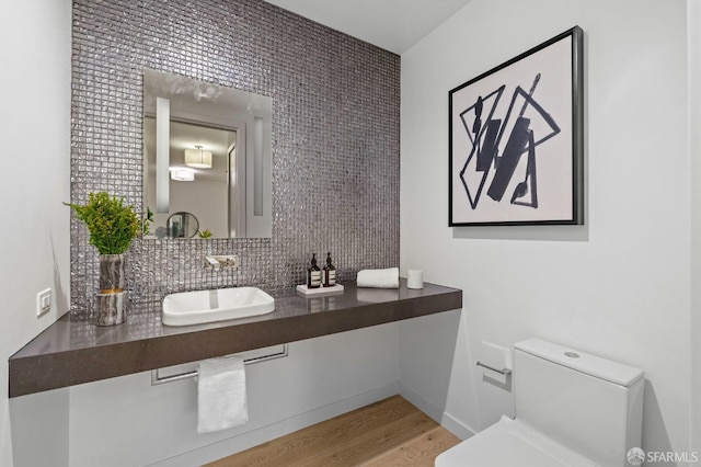 bathroom with toilet, sink, hardwood / wood-style floors, and backsplash