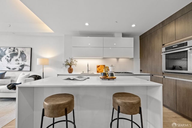 kitchen featuring sink, a kitchen breakfast bar, stainless steel oven, and white cabinets