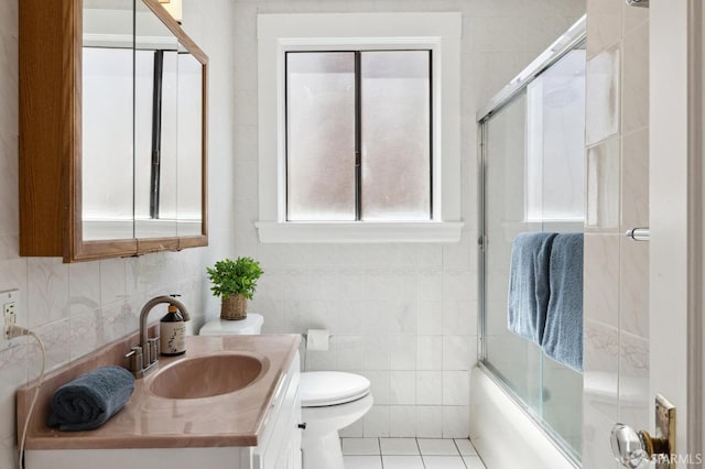 full bathroom featuring tile patterned floors, bath / shower combo with glass door, toilet, vanity, and tile walls