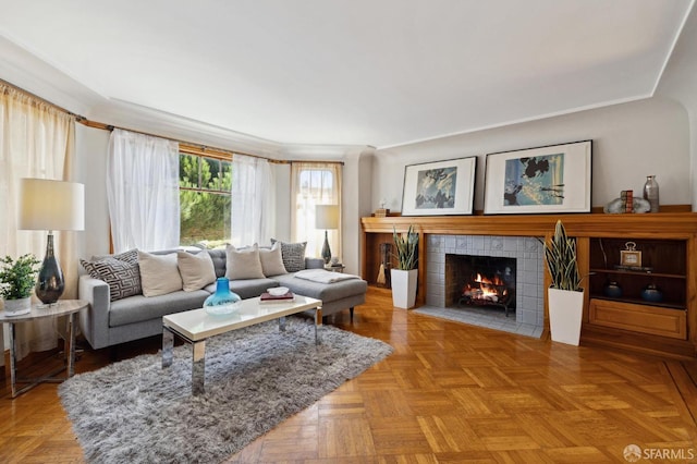 living room with a tile fireplace, crown molding, and light parquet flooring