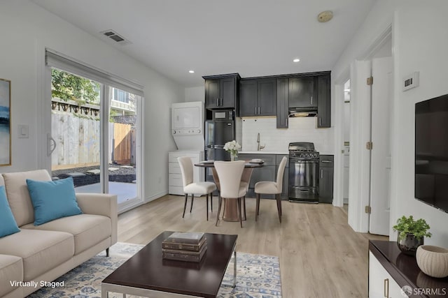 living room with visible vents, light wood-type flooring, stacked washer and clothes dryer, and recessed lighting