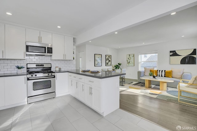 kitchen with white cabinets, dark countertops, appliances with stainless steel finishes, a peninsula, and decorative backsplash