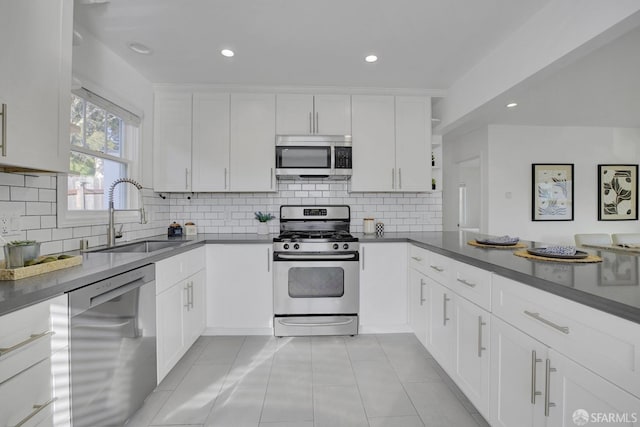 kitchen featuring white cabinets, a sink, dark countertops, stainless steel appliances, and light tile patterned flooring