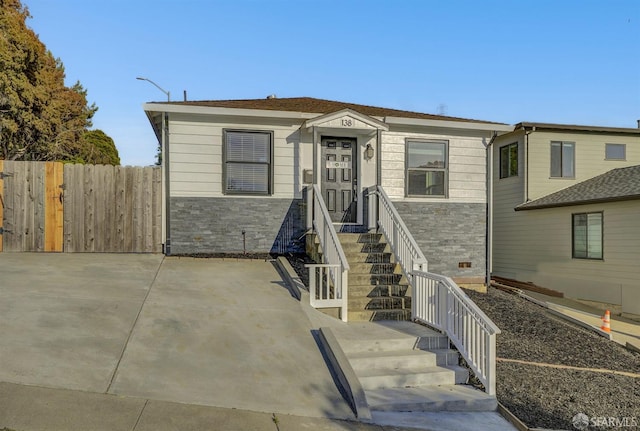 view of front of house featuring entry steps, stone siding, and fence