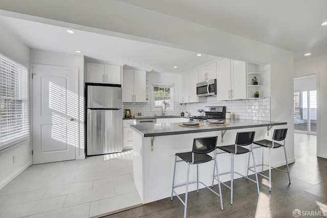 kitchen with stainless steel appliances, a peninsula, open shelves, and dark countertops