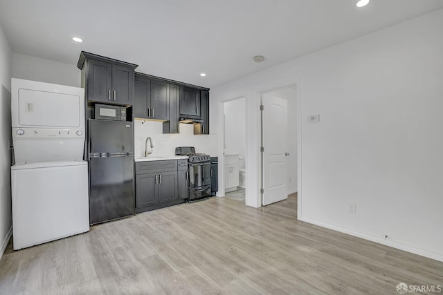 kitchen with stacked washer and clothes dryer, light countertops, under cabinet range hood, light wood-style floors, and black appliances